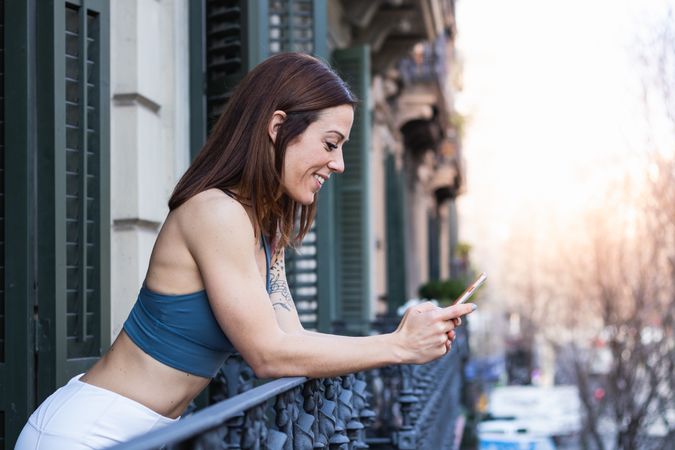 Smiling sportswoman chatting on smartphone on balcony