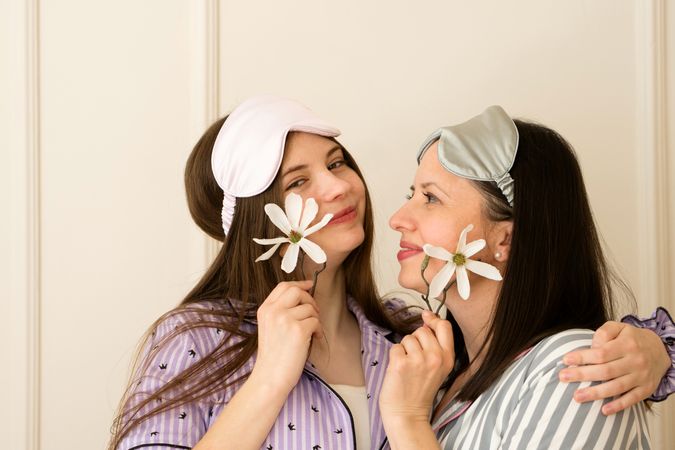 Mother and daughter in pajamas holding flowers to cheeks