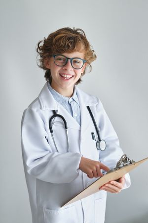Smiling boy in medical uniform pointing at clipboard