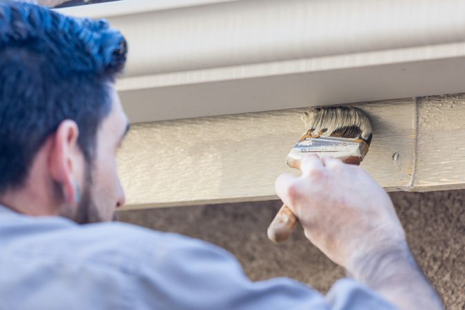 Professional Painter Using Brush to Paint House Fascia Under Rain Gutter