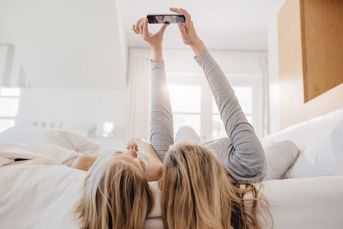 Woman taking selfie with little girl and hanging off bed