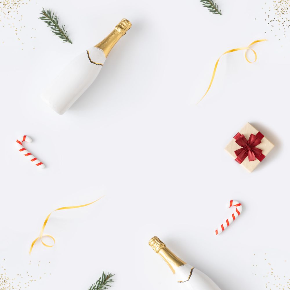 Holiday decorations; Champagne, candy cane and present arranged at top border of light background