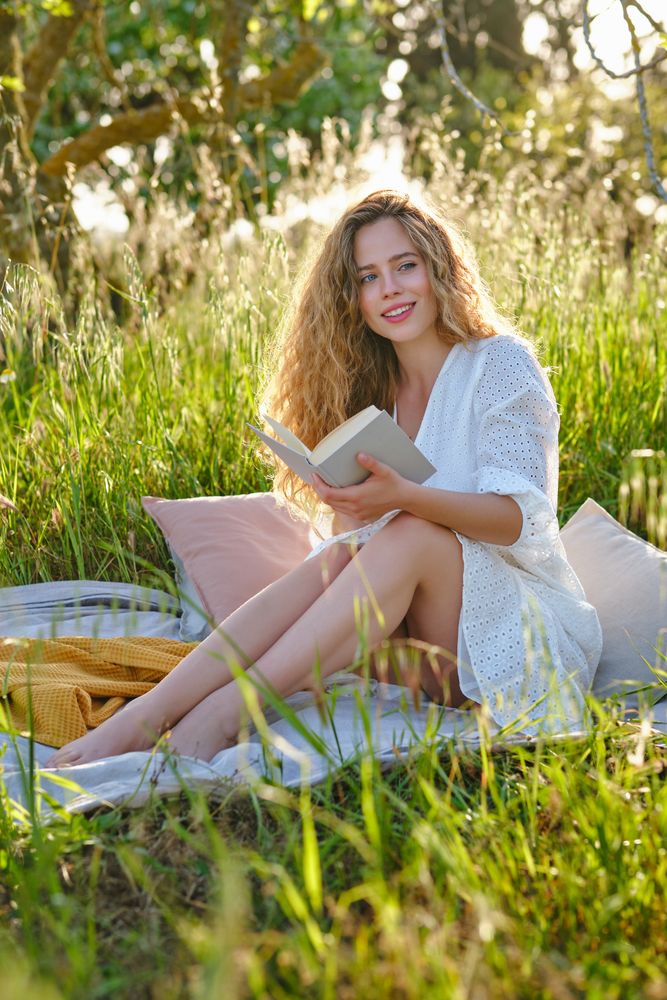 Cheerful woman reading book on grassy lush glade