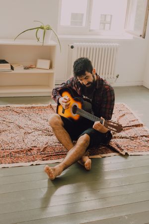 Relaxed bearded man playing guitar at home