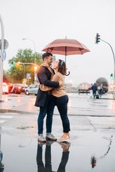 Happy couple with umbrella hugging on wet street