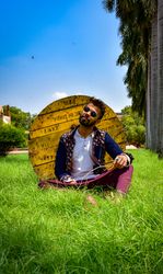 Man in traditional outfit sitting on green grass beside wooden spool
