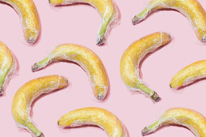 Plastic wrapped bananas on pink background