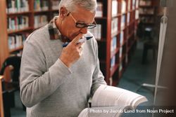 Mature man reading a book with concentration standing in classroom 0y6ZL5