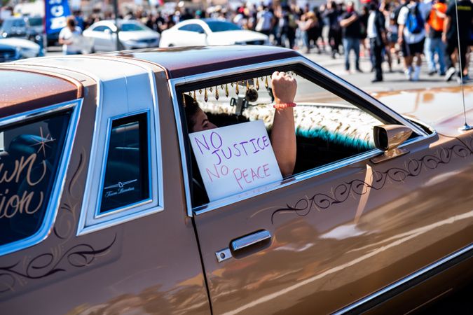 Los Angeles, CA, USA — June 7th, 2020: woman riding in car with “no justice no peace” protest sign