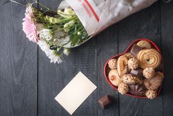 Top view of heart-shaped box with sweets, bouquet of flowers and blank message card on rustic table