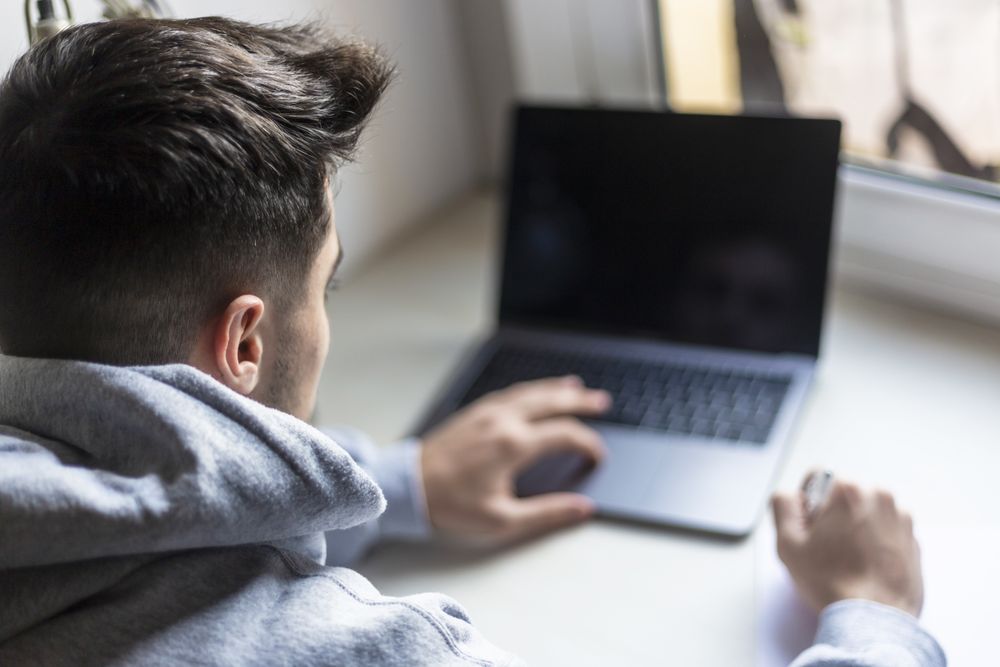 Rear view of a male working on laptop by window at home