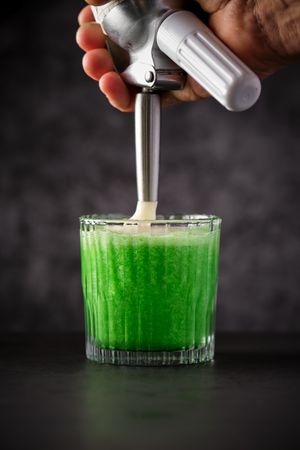Crop bartender adding whipped foam to delicious cocktail with cr