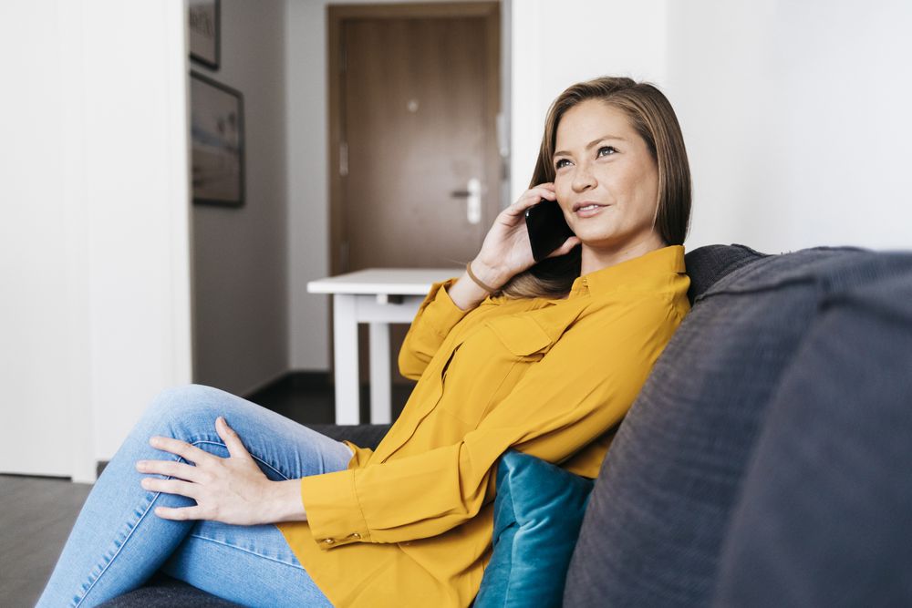 Beautiful adult female sitting on sofa while talking on smartphone