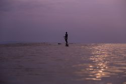 Man with paddle on surf board between waving water at sunset