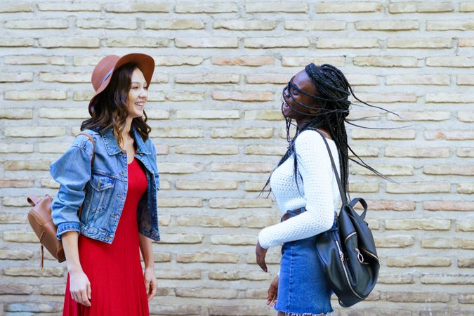 Two women facing each other and chatting beside a brick wall