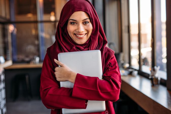 Cheerful Muslim woman in hijab with laptop computer looking at camera and smiling
