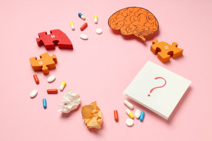 Pink paper circle flat lay with pills, puzzle pieces, brain and question mark with copy space