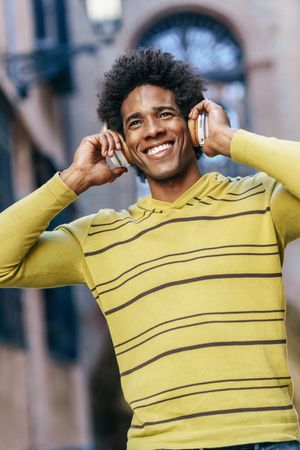 Man walking and smiling outside wearing headphones, vertical
