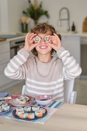 Cheerful boy having fun with sushi in kitchen