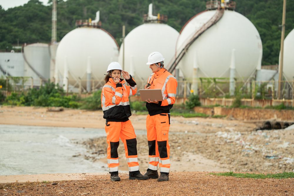 Two engineers are working at an industrial site near spherical gas storage tanks.