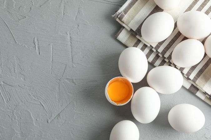 chicken eggs in kitchen towel on grey background, space for text and top view