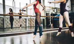 Crop women in bodysuits jumping on pointe above floor in studio training ballet.