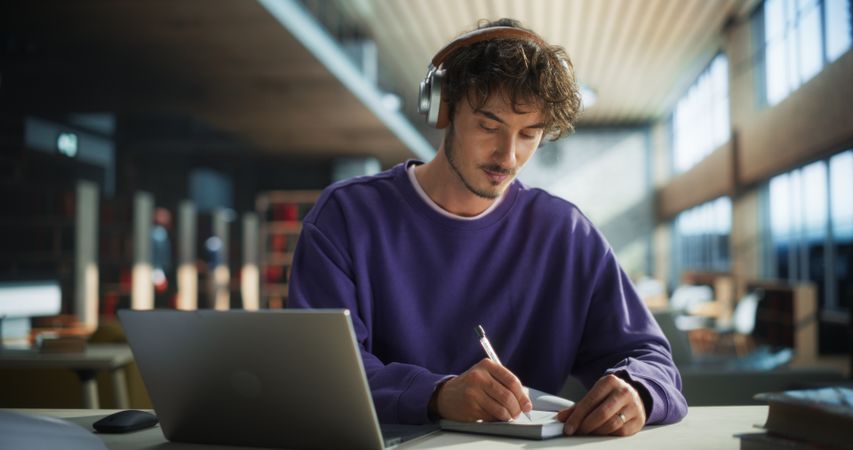 Thoughtful Young Student Preparing for Class, Doing Homework on a Laptop Computer. Freelance Journalist Working on an Article in a Public Library with Modern Simple Interior