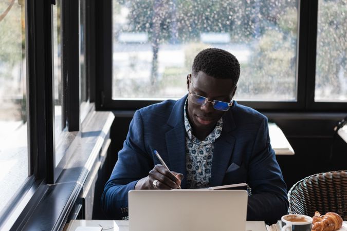 Focused Black male entrepreneur taking notes during work in cafe