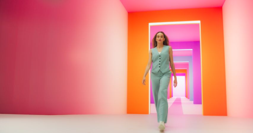 Low Angle Portrait of a Fashionable Young Woman Performing a Catwalk in a Colorful Neon Studio. Stylish Female Walking Confidently in Bright Lit Room, Working as A Model For Luxurious Fashion Brand