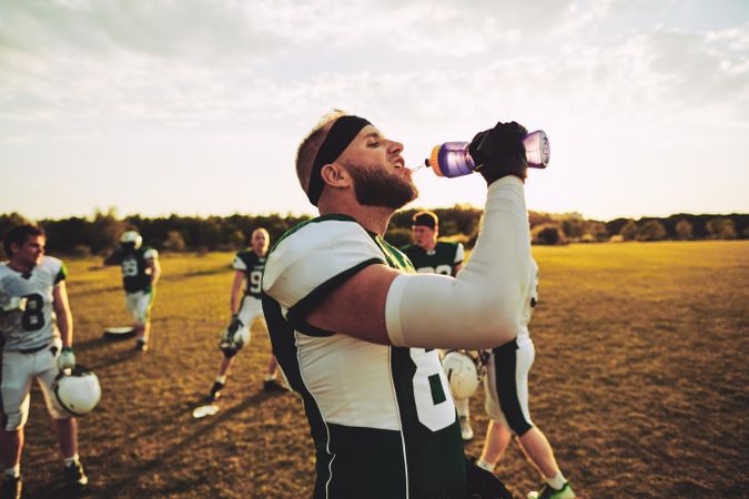 Man squeezing water bottle into mouth after a football game