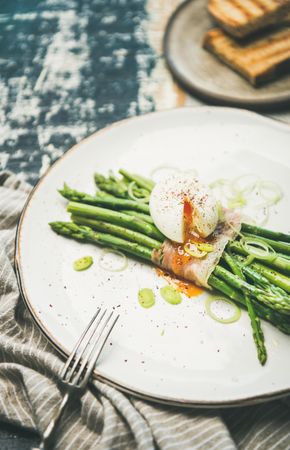 Asparagus and soft boiled egg on plate with fork, on wooden table, with linen