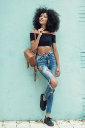 Female wearing casual clothes leaning on turquoise wall and looking around