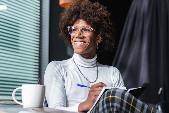 Happy trendy young Black guy doing assignment in cafe