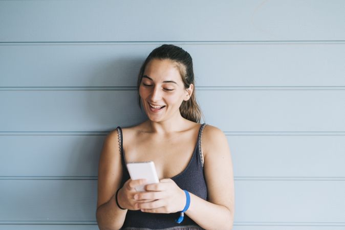 Smiling teenage female texting on cell phone while leaning against wood paneled wall