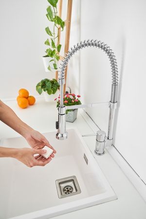 Crop person washing hands with soap in sink