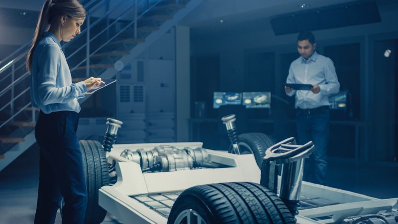 Team of Automotive Engineers Working on Electric Car Chassis Platform, Taking Measures, working with 3D CAD Software