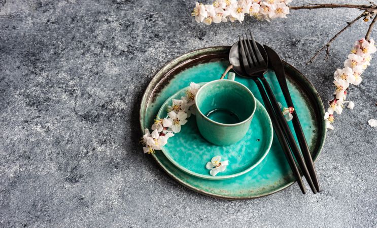 Spring floral concept with top view of apricot blossom branches surrounding teal plates on grey table