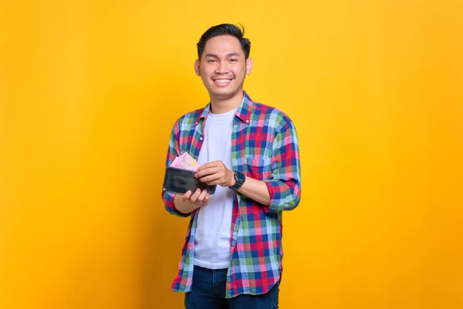 Happy Asian man smiling while taking cash out of his wallet