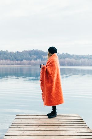 Woman wrapped in orange blanket looking out over lake