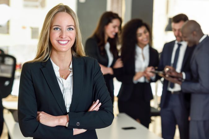 Blonde businesswoman standing in foreground of busy office