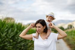 Adorable kid in hat on shoulders and looking at mother
