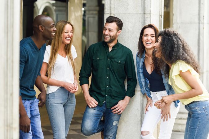 Group of women and men chatting together by city pillar