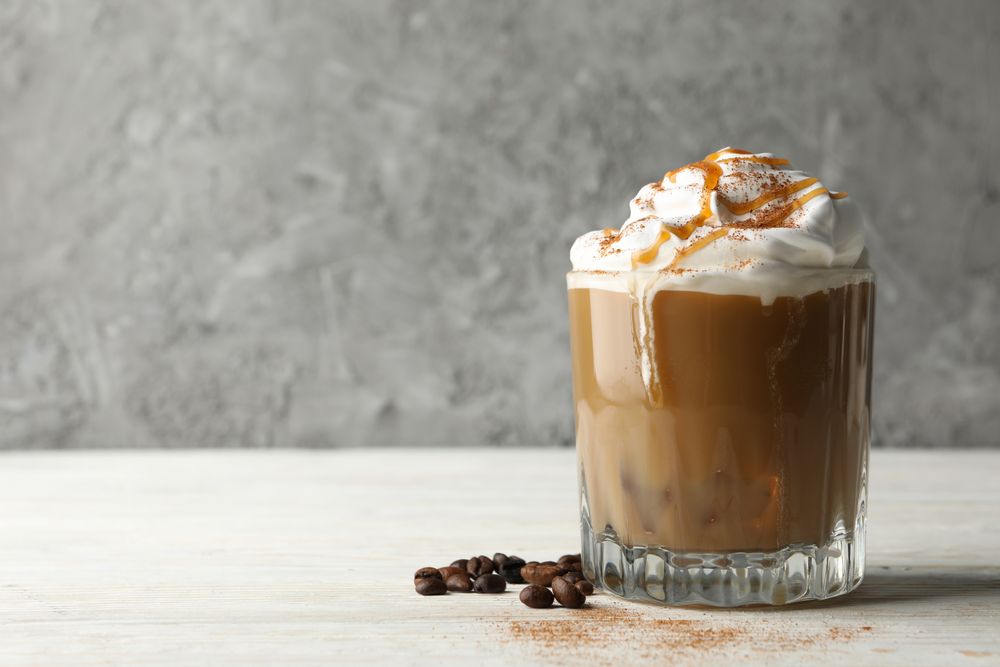 Glass of ice coffee with poured cream on wooden table