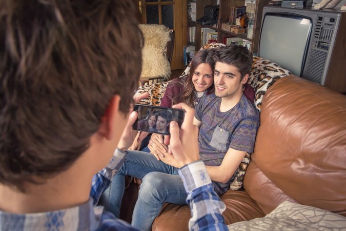 Friend taking photos to cute couple on a sofa
