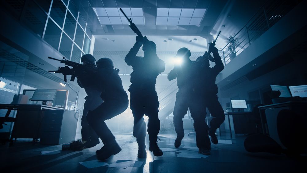 Masked Team of Armed SWAT Police Officers Move in a Hall of a Dark Seized Office Building with Desks and Computers.
