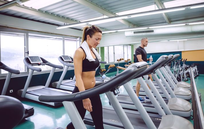 Fit male and female warming up on treadmills in gym