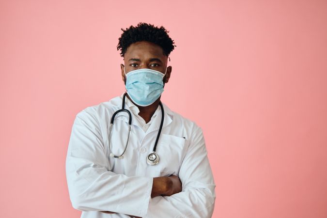 Black male doctor in pink studio with stethoscope and facemask