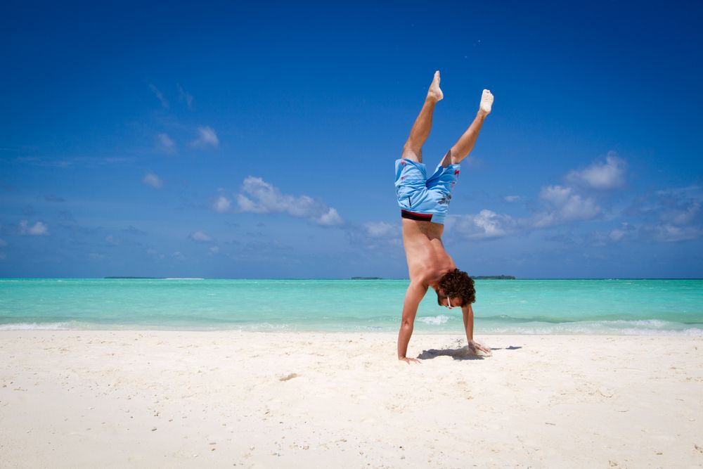 Unrecognizable male standing upside down near turquoise sea