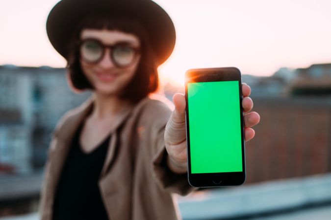 Smiling woman with glasses and hat with smart phone outside
