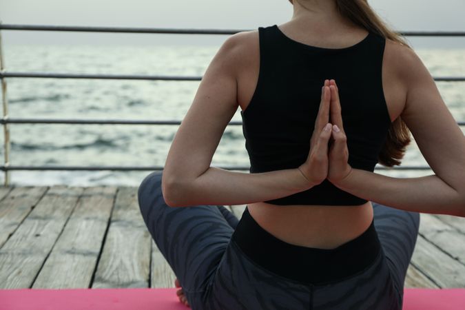 Young woman on yoga mat on wooden floor outdoors, space for text